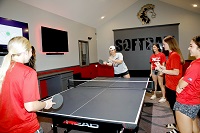 Members of the EMCC softball team now have a dedicated facility that includes a combination recreation and lobby area, locker rooms and enclosed pitching and hitting lanes. Here, Sasha King serves during a game of ping pong with Rachel Rommell in the building’s recreation area while other members of the softball team look on. 